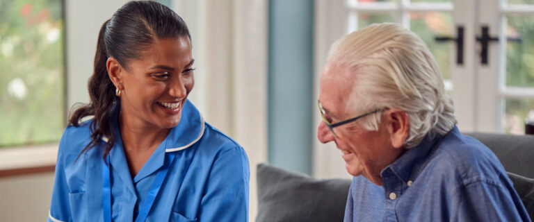 An elderly man laughs together with his home health aide as they go through memory care exercises together in his living room.