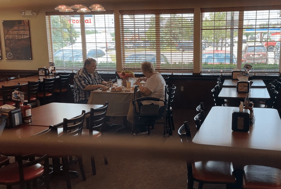 An elderly couple sits in an empty dining room at the Golden Corral, sharing a meal together.