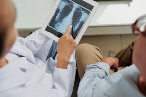 A doctor goes over a recent home xray with a patient, pointing out areas of interest on the xray which has been brought up on a tablet.