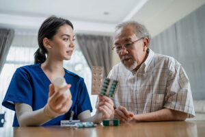 A skilled nursing assistant walks an elderly man through his medication regiment while holding up pills and explaining when to take them.