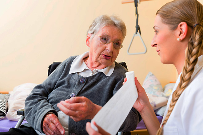 A visiting doctor unrolls a length of gauze to help an elderly woman change the dressings on her wound.